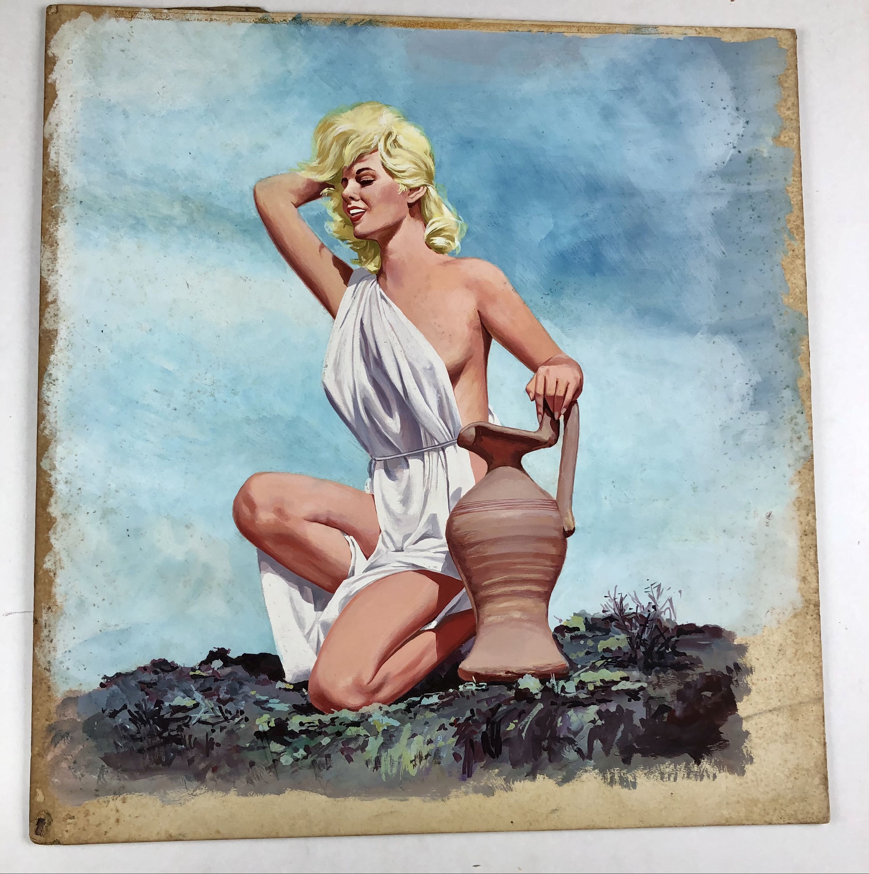Bunny Yeager, model, in toga kneeling next to clay vase against blue sky