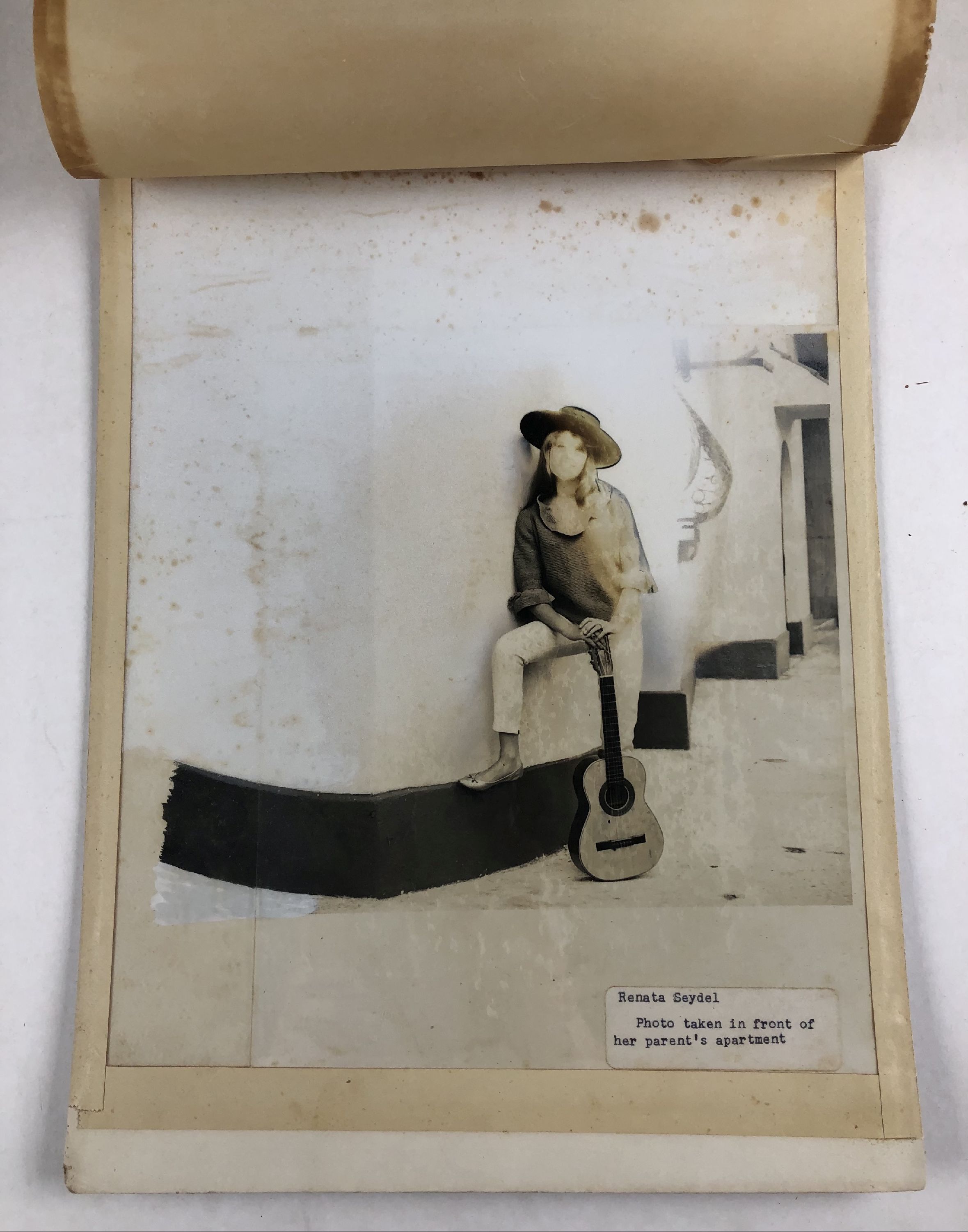 mechanical reproduction with applied handwork of woman standing against a wall with a guitar. Caption reads "Renata Seydel: Photo taken in front of her parent's apartment"