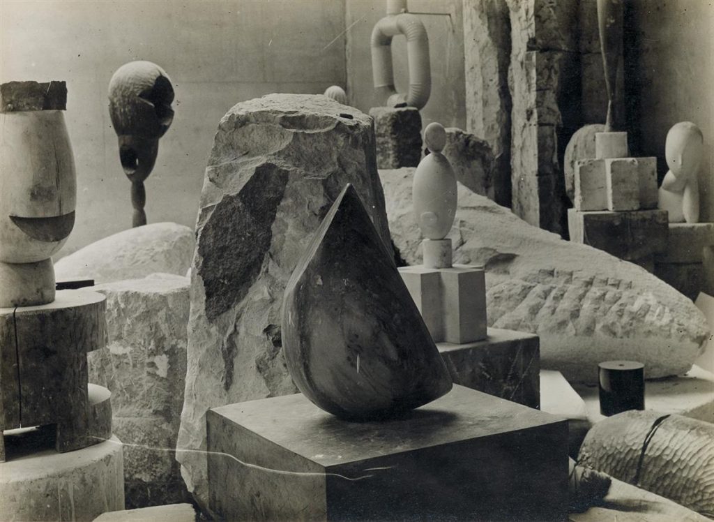 A black and white photograph by Constantine Brancusi of four of his most iconic sculptures in his studio.