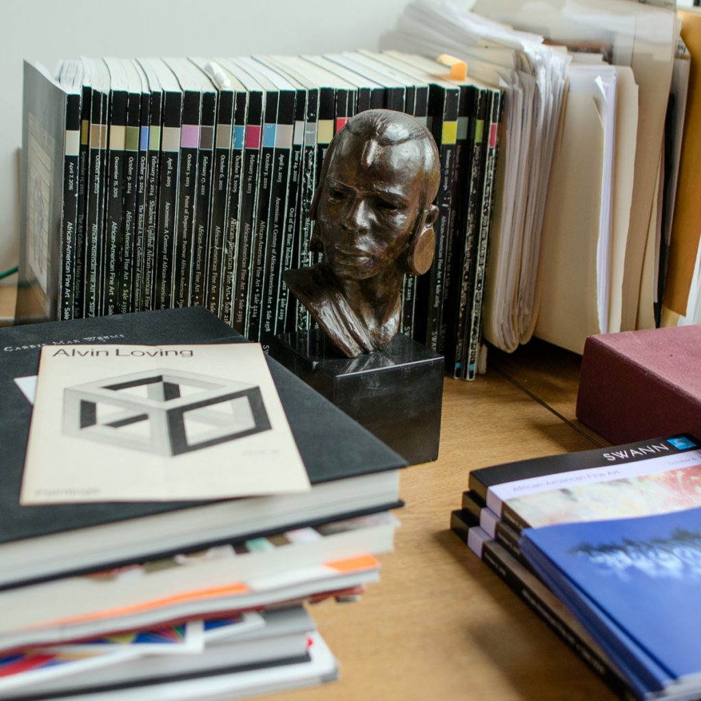 A bust sculpture by Elizabeth Catlett surrounded by auction catalogues and books.