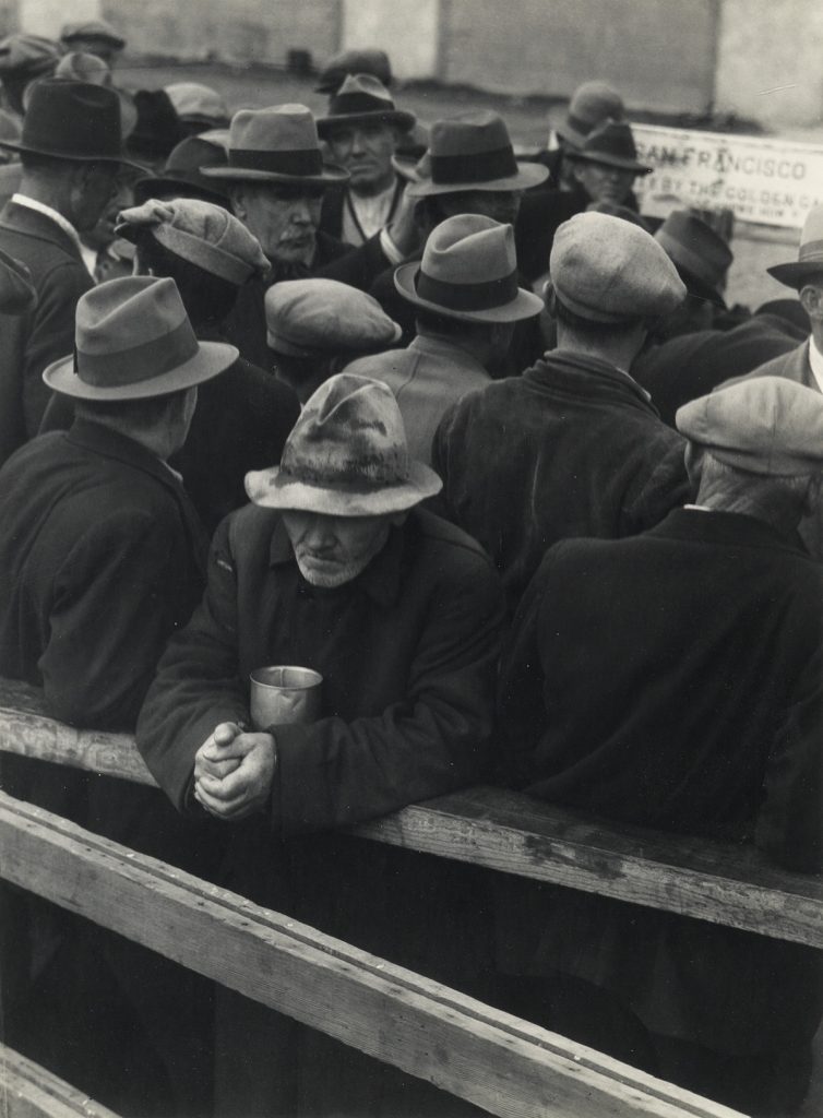 Black and white image of men waiting in a breadline during the Great Depression by Dorothea Lange.