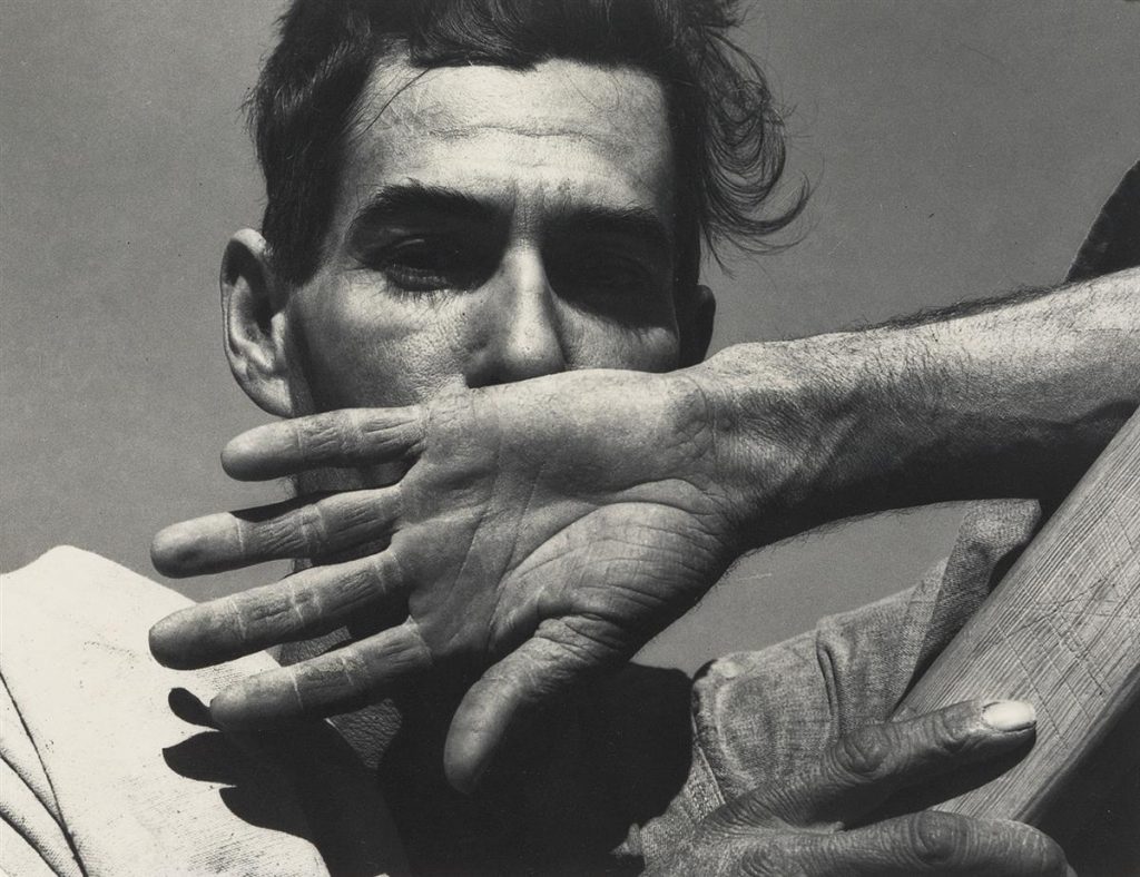 Black and white photographic portrait of a man covering his face with the back of his hand.