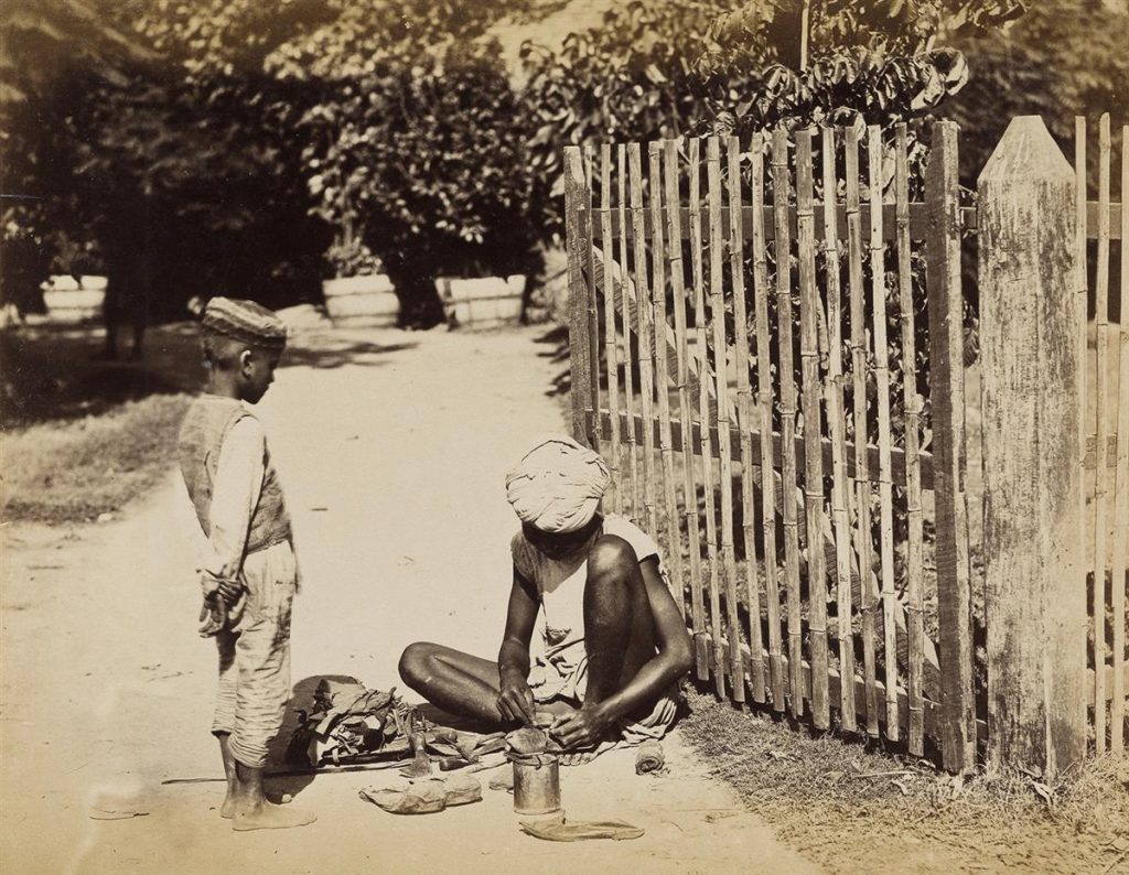 Image of a young Indian boy and teen sitting on the streets of India in the 1870s. 