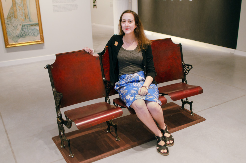 Lauren Goldberg sits in old theater chairs at the Poster House museum's Alphonse Mucha exhibition.