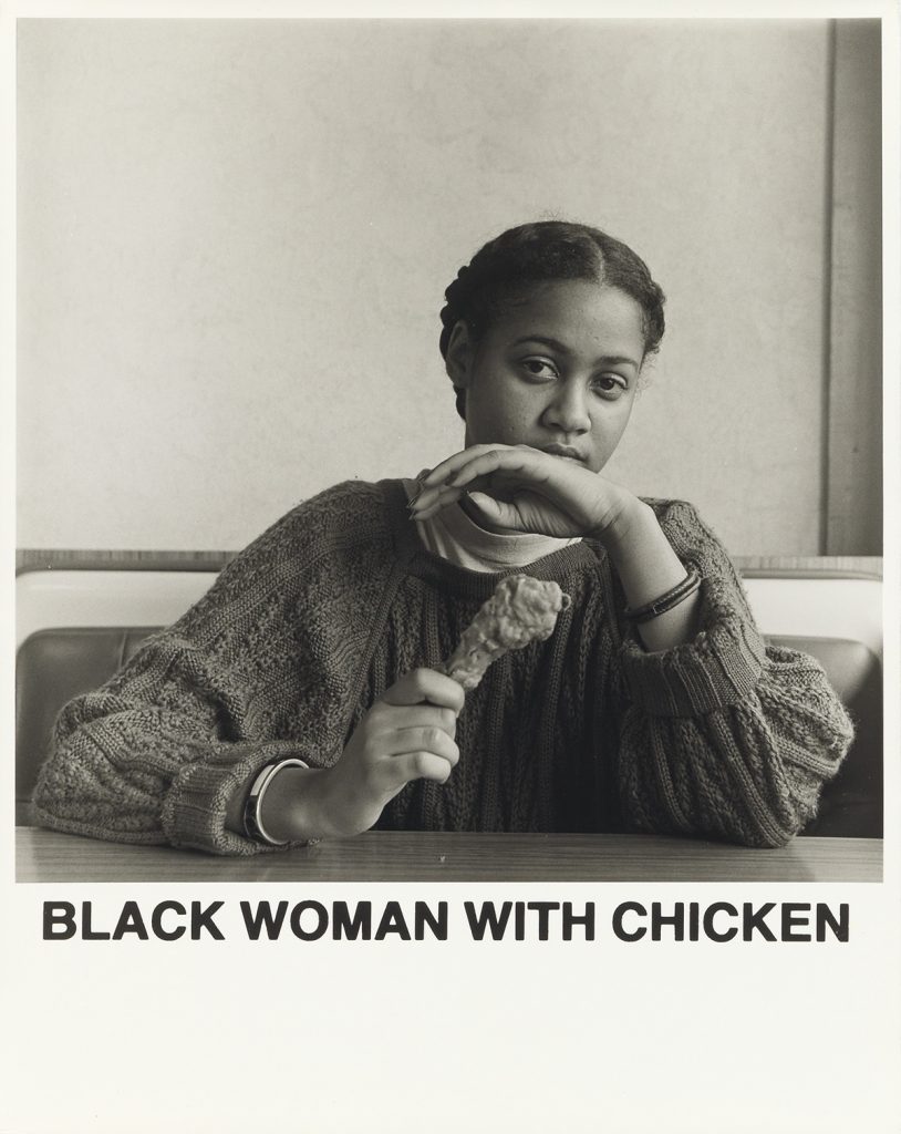Carrie Mae Weems, Black Woman with Chicken, black and white silver print of a woman holding a chicken leg, with text that reads "Black Woman with Chicken," 1987.